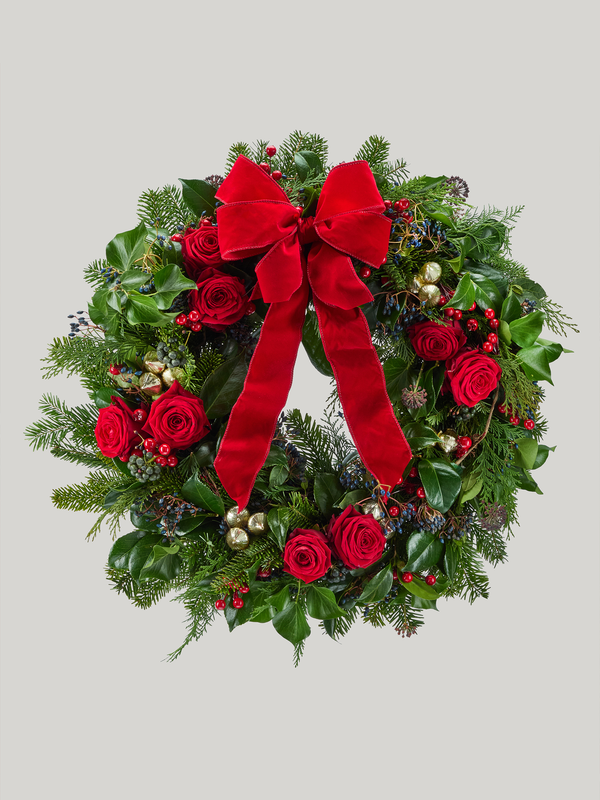 Christmas wreath with red roses, berries, and a large red bow on a light gray background