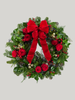 Christmas wreath with red roses, berries, and a large red bow on a light gray background
